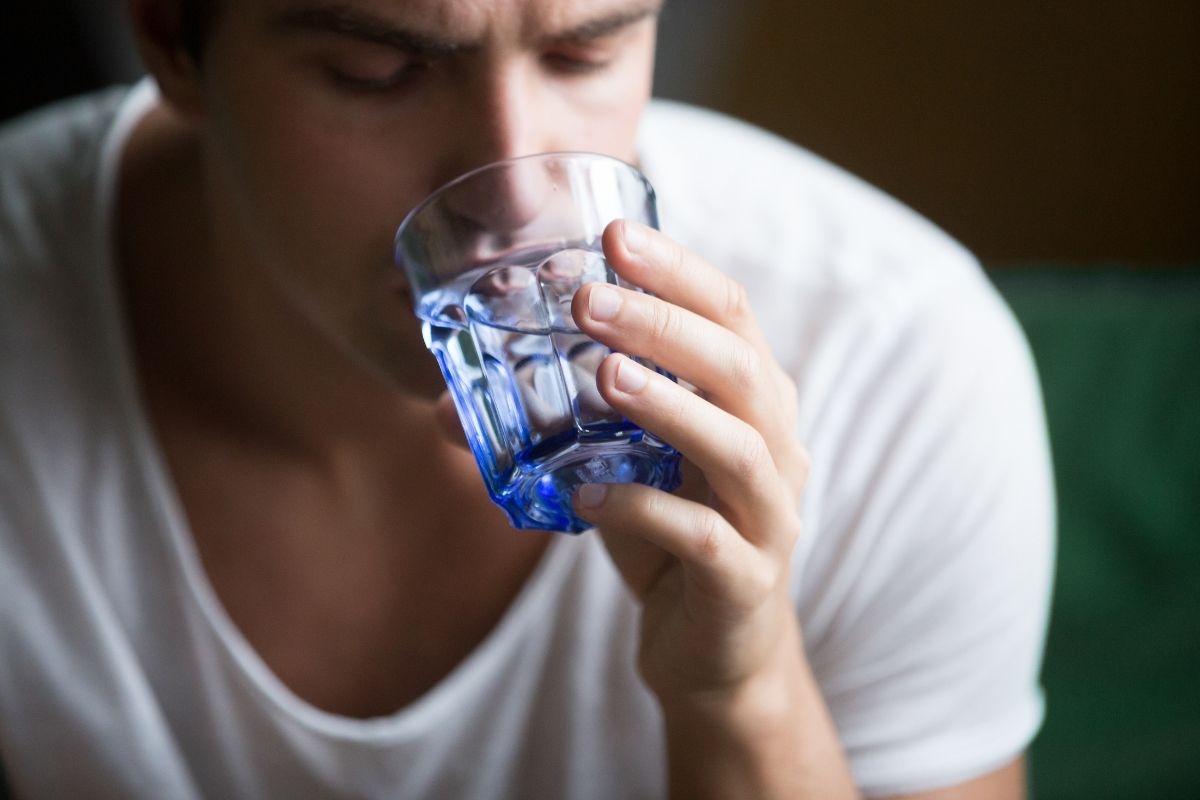 man drinking a glass of water due to dehydration