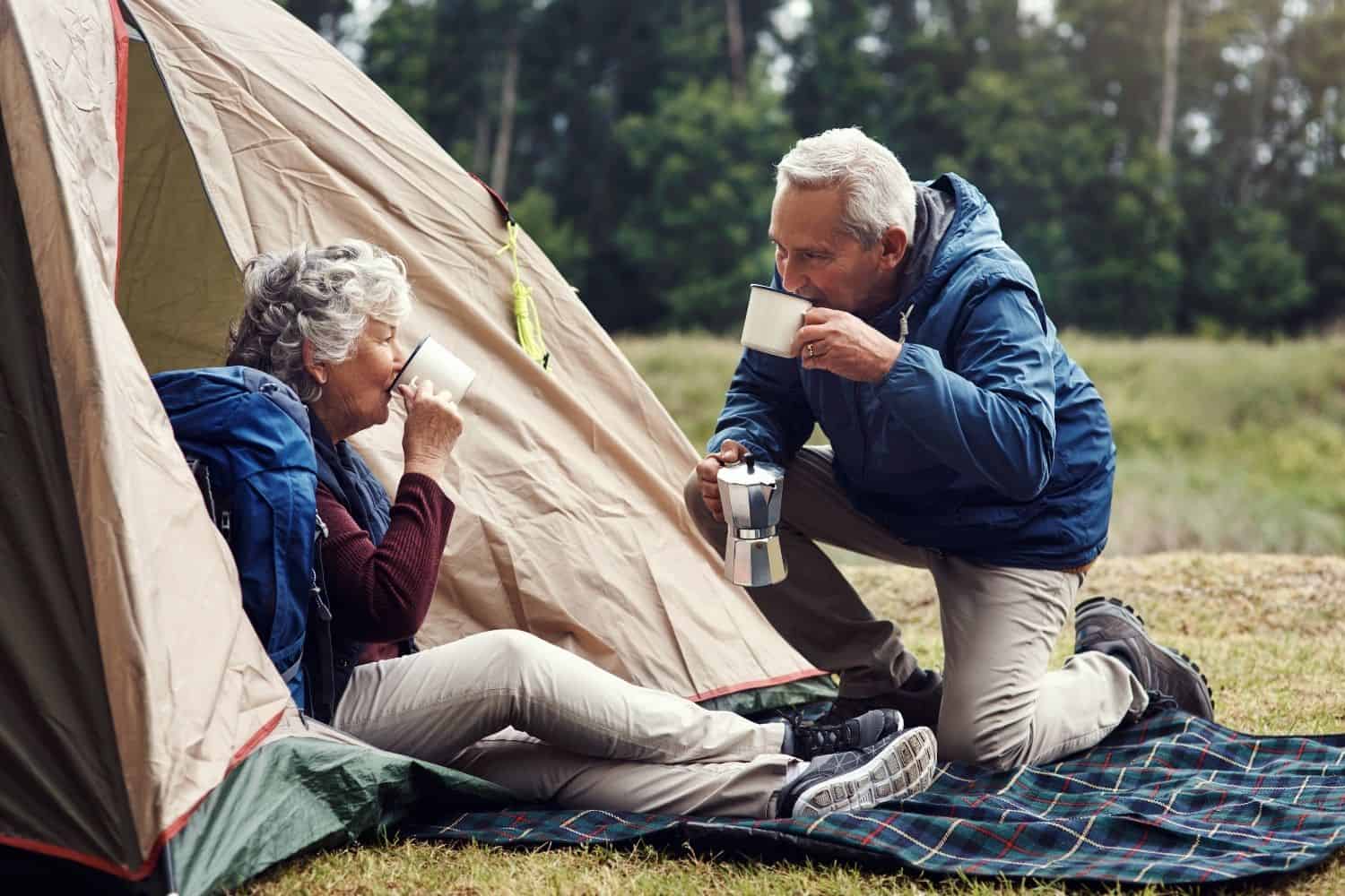 old couple drinking coffee outside their camping tent.