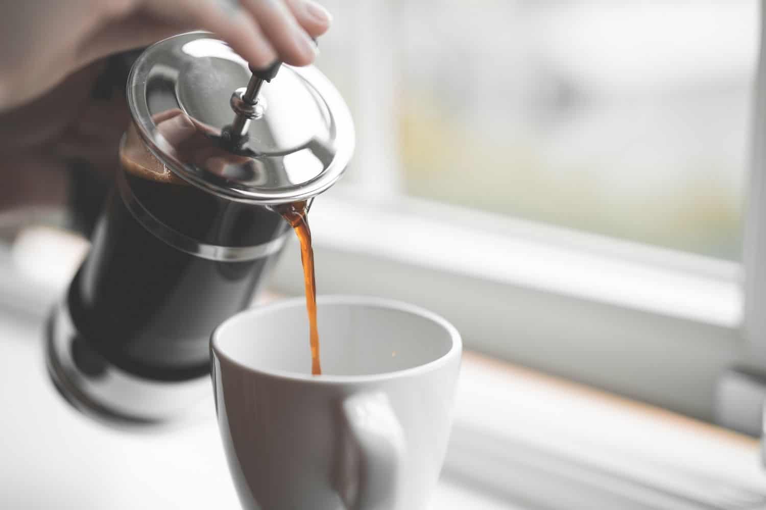 woman pouring french press coffee into a cup.