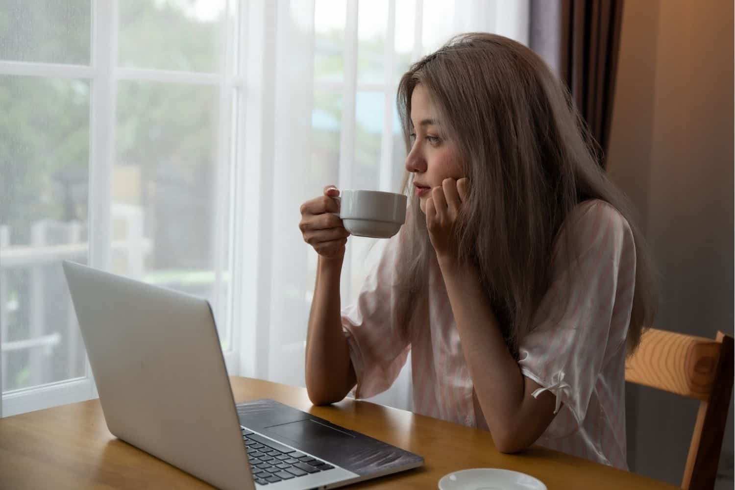 young woman drinkng a cup of coffee while working from home.