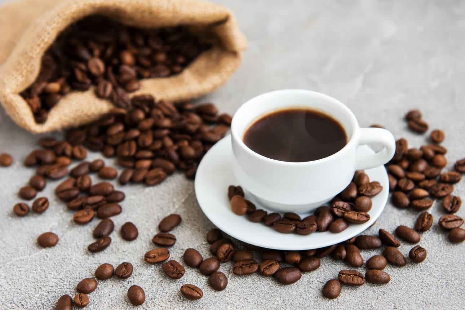 black coffee in a cupnext to a bag of coffee beans.