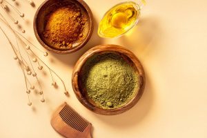 oil in white cup, henna and coffee grinds in wooden bowl with a wooden comb