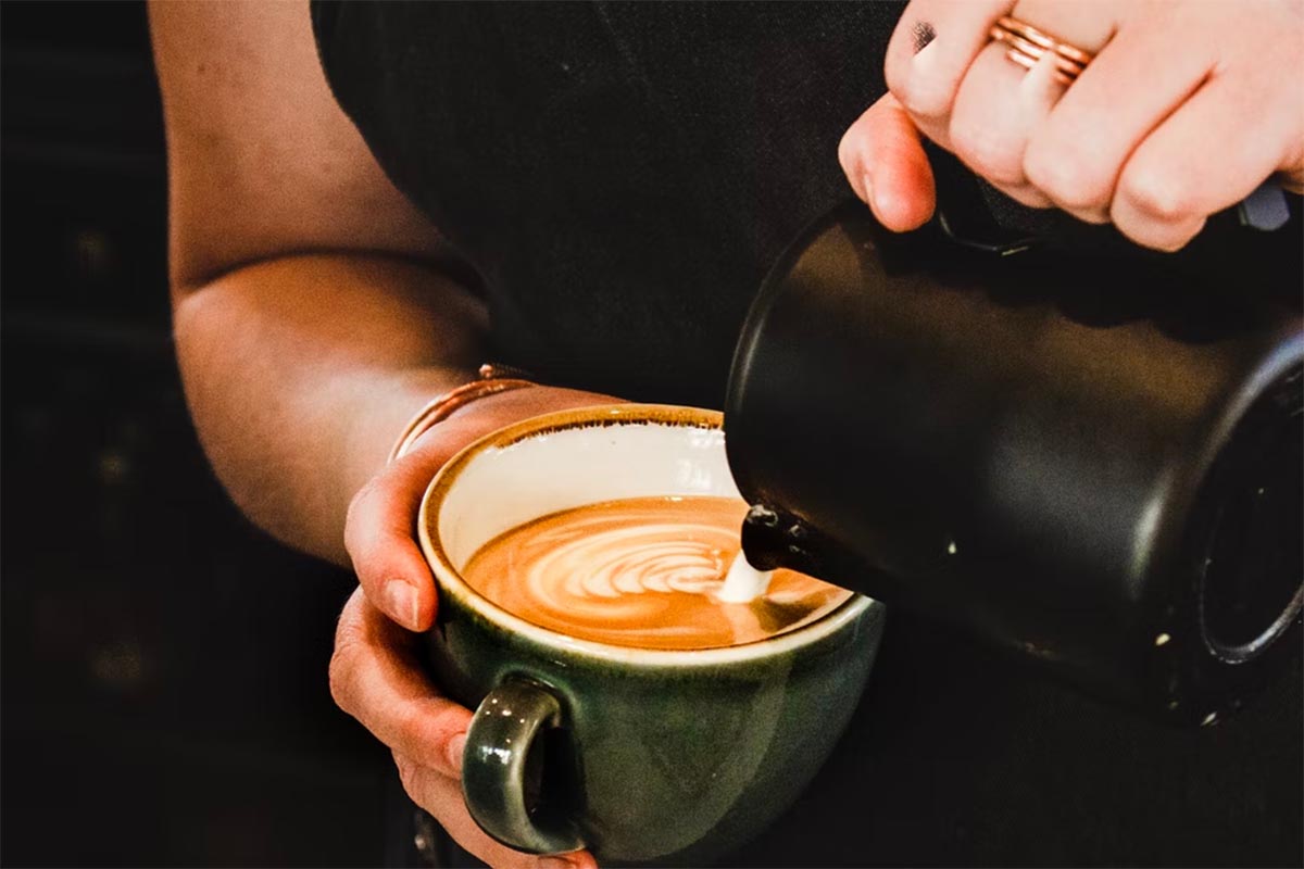 person pouring cappuccino on gray mug