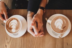 two cup full of coffee and two hands holding each other